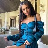 Woman in a teal off-the-shoulder dress with puff sleeves and a sweetheart neckline, sitting on a couch.