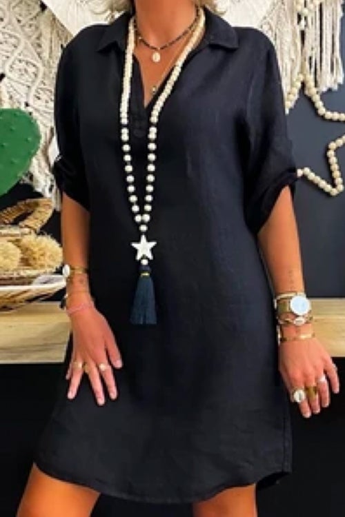 Woman wearing a black collared V-neck short sleeve A-line dress with a long beaded necklace with a star and tassel pendant.
