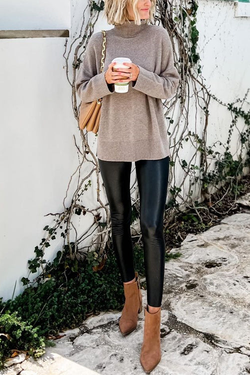 A woman wearing a taupe mock neck sweater and black faux leather leggings.
