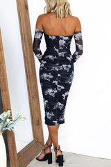 Back view of a woman in a black and white floral print off-the-shoulder ruched mesh midi dress with sheer long sleeves.