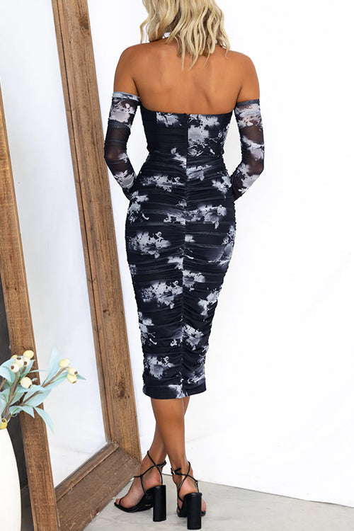 Back view of a woman in a black and white floral print off-the-shoulder ruched mesh midi dress with sheer long sleeves.
