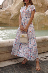 A woman wearing a white midi dress with a playful print of abstract shapes, faces, and red lipstick marks, standing in front of a fountain.