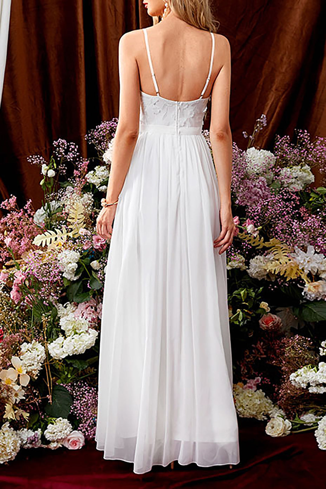 Back view of a woman in a white wedding dress with thin straps and a flowing skirt.