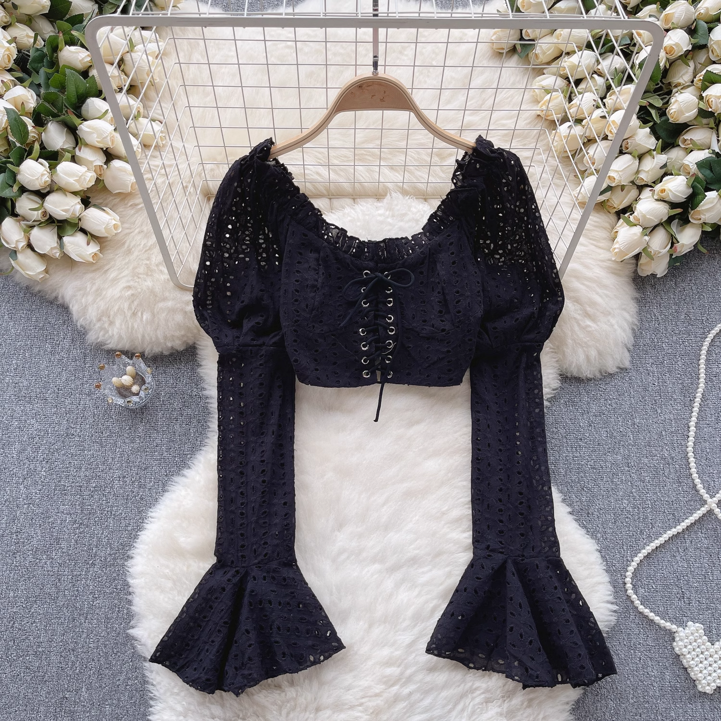 A black eyelet lace crop top with long puff sleeves and flared bell sleeves, styled with decorative elements.