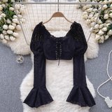 A black eyelet lace crop top with long puff sleeves and flared bell sleeves, styled with decorative elements.
