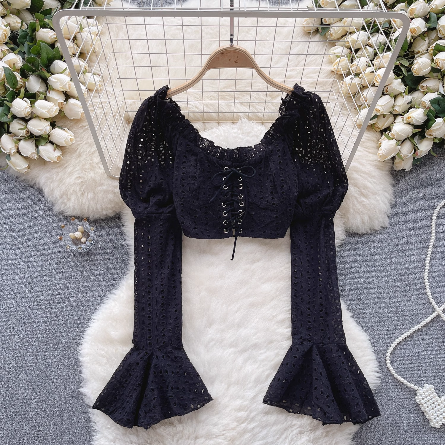A black eyelet lace crop top with long puff sleeves and flared bell sleeves, styled with decorative elements.