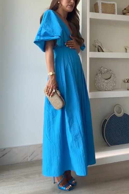 Side view of a woman in a blue maxi dress and gold clutch.