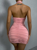 The back of a woman wearing a pink ruched halter neck mini dress with a cut-out detail.