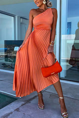 A woman in an orange one-shoulder pleated dress with a cut-out detail and a red handbag.