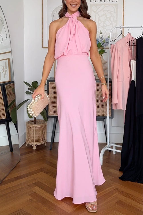 A woman models a pink halter neck gown, showcasing the flowing skirt.