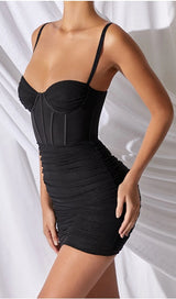 Side view of a woman wearing a black ruched mini dress with a corset bodice
