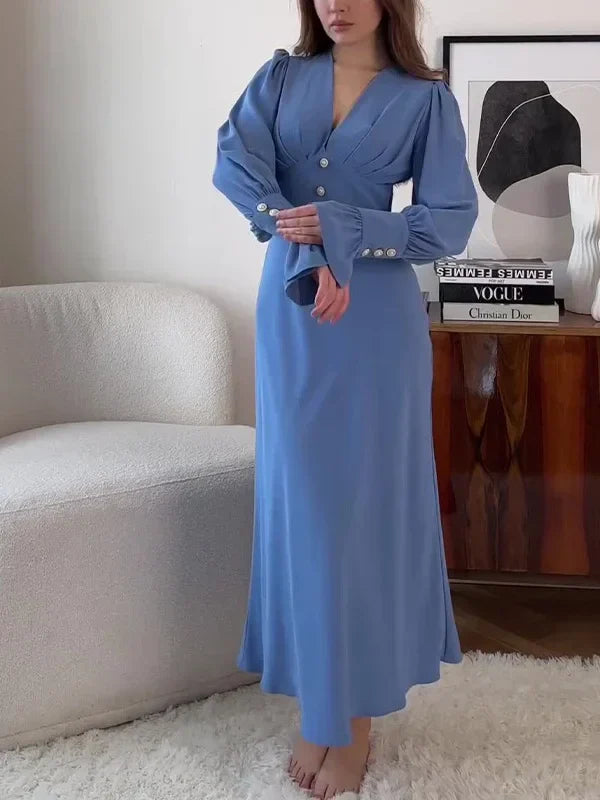 Woman wearing a long-sleeved blue dress with puffed sleeves and a V-neckline, standing in a room.
