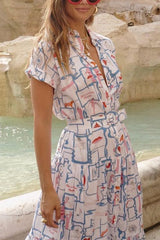 A woman in a printed shirt dress with a tiered skirt and a belt, accessorized with sunglasses and jewelry.