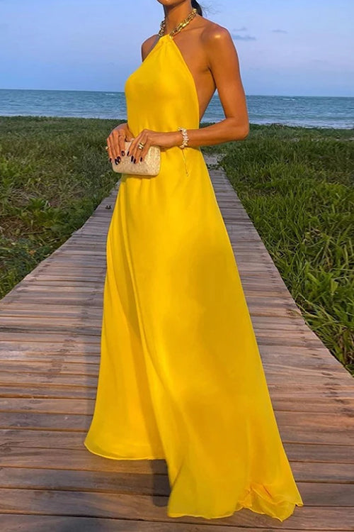 woman wearing a long yellow halter neck dress with a flowy skirt and a clutch on a boardwalk
