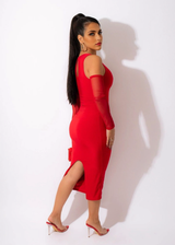 A woman in a red midi dress with sheer sleeves and a side slit, viewed from the side.