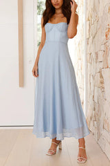 A woman posing in a light blue midi dress, holding the skirt slightly.