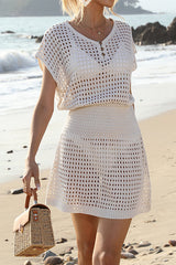 Woman wearing a white crochet knit mini dress with short sleeves and a cinched waist, standing on a beach.