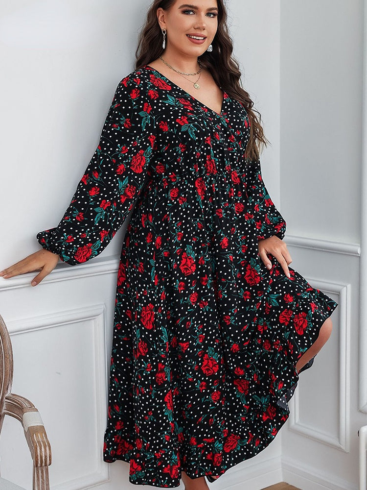A plus-size woman leaning against a wall, wearing a black floral and polka dot midi dress.