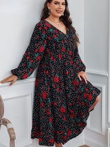 A plus-size woman leaning against a wall, wearing a black floral and polka dot midi dress.