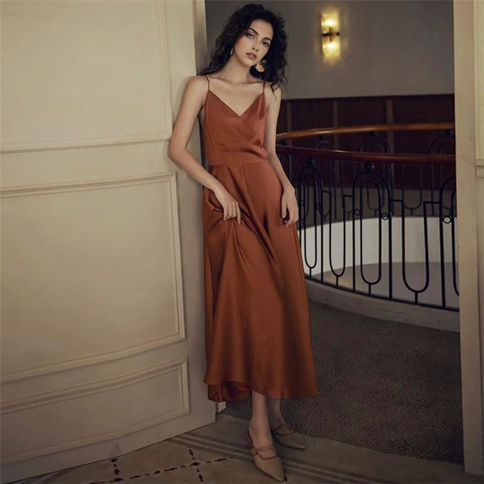 Woman leaning against a wall, wearing a burnt orange satin dress