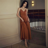 Woman leaning against a wall, wearing a burnt orange satin dress