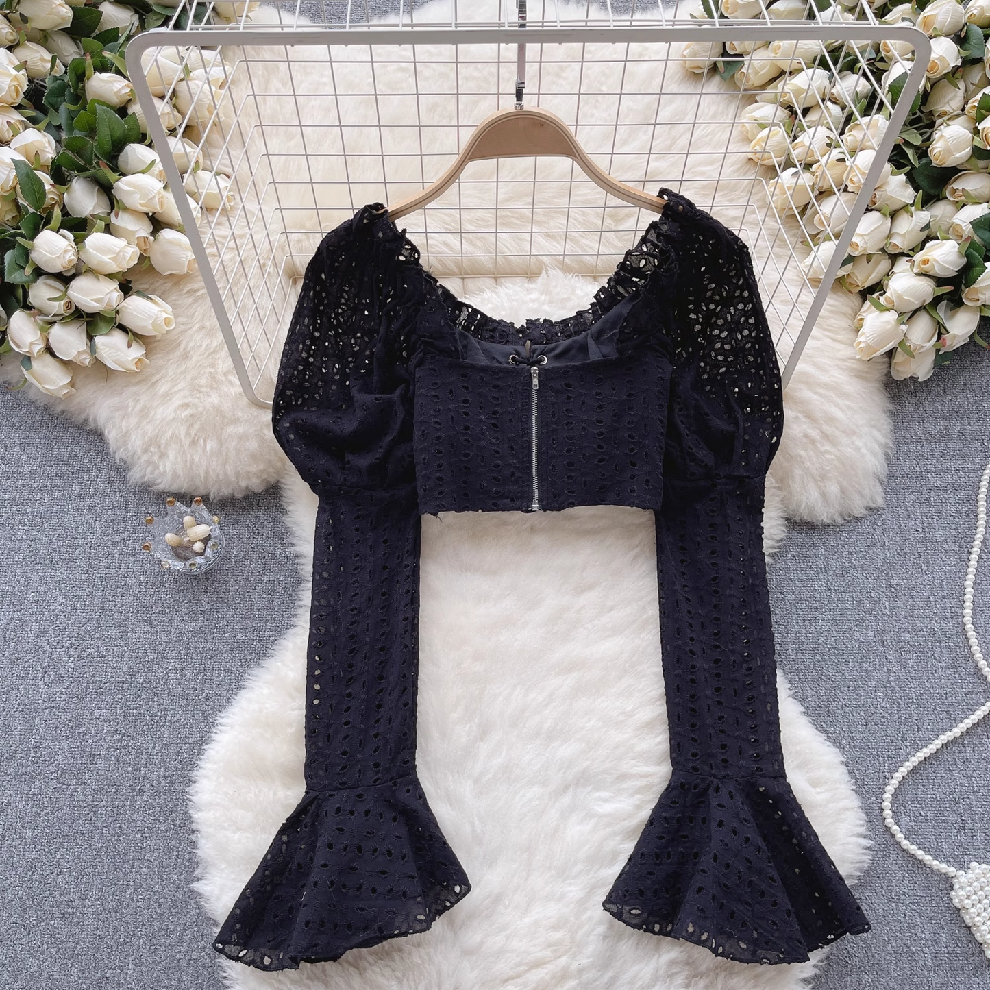 A black eyelet lace crop top with a zipper closure on the back, featuring puff sleeves and bell sleeves.