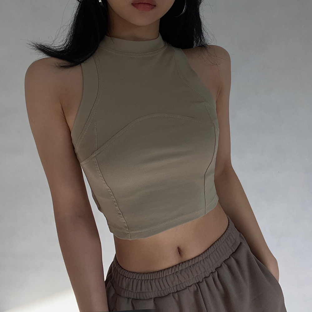 Woman wearing a beige cropped tank top and brown sweatpants, showing her midriff.