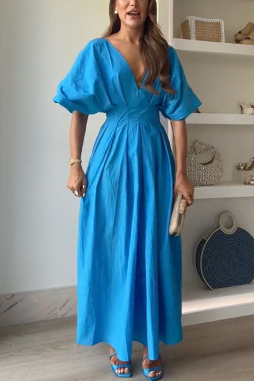 Woman in a blue maxi dress with voluminous sleeves and a pleated skirt.