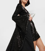 side view of a woman wearing a black sequined mini dress with long bell sleeves and a draping high-low hem