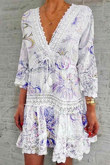 A woman modeling a white bohemian-style dress with purple floral print and lace trim.