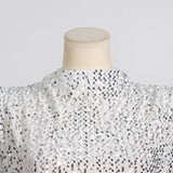 Close-up of the sequined fabric and high neckline of a white dress on a mannequin.