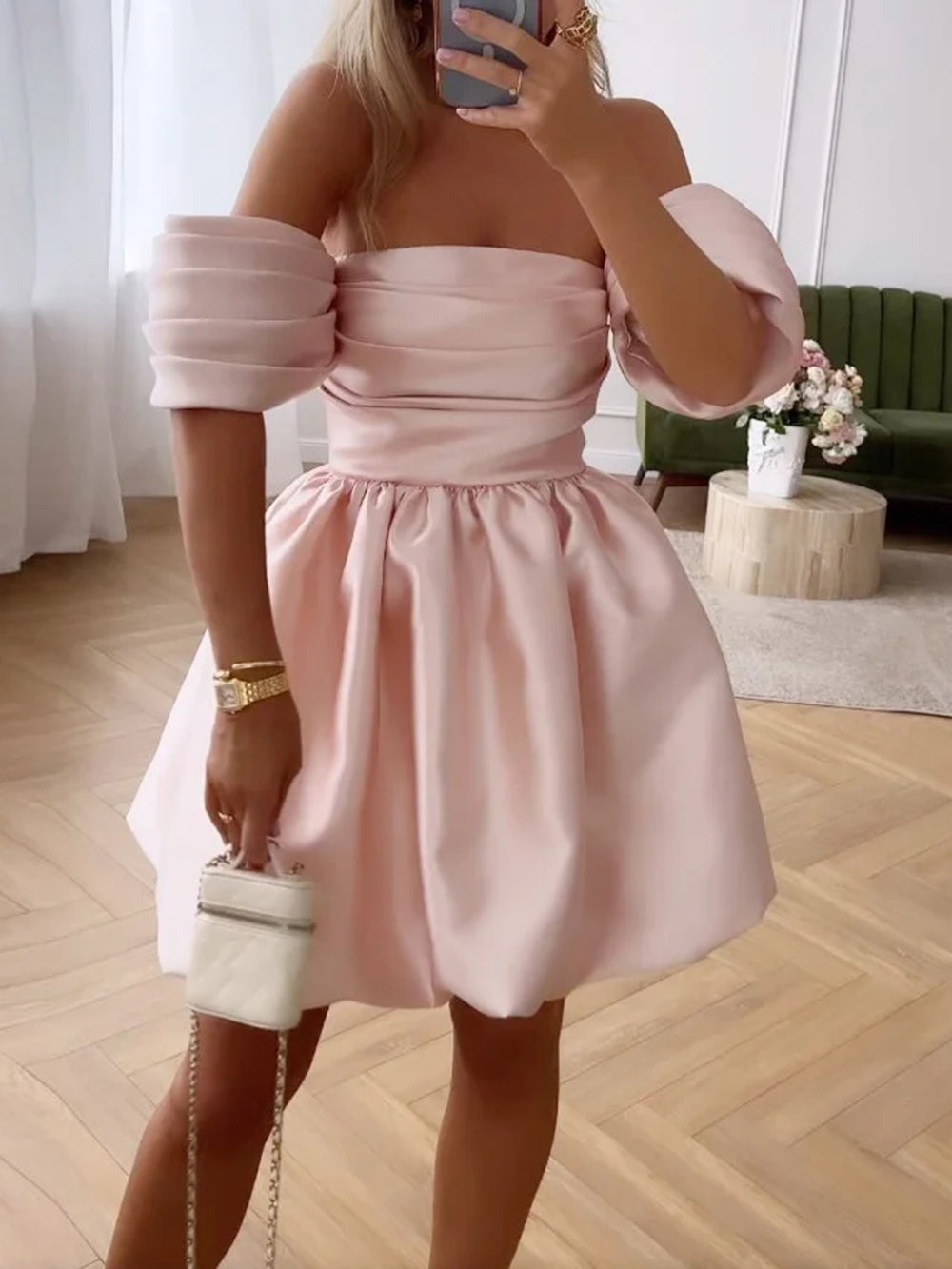 woman in a pink off-the-shoulder mini dress with puffy sleeves and a bubble skirt, holding a white clutch
