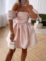 woman in a pink off-the-shoulder mini dress with puffy sleeves and a bubble skirt, holding a white clutch