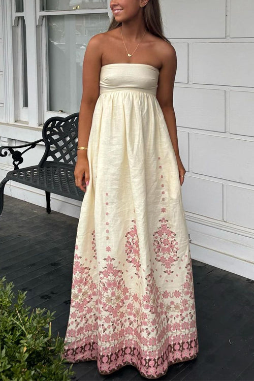 A woman smiling while wearing a cream strapless maxi dress with a pink floral print.
