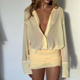 A woman in a pale yellow sheer button-down shirt and ruched mini skirt, showing the deep V-neck.