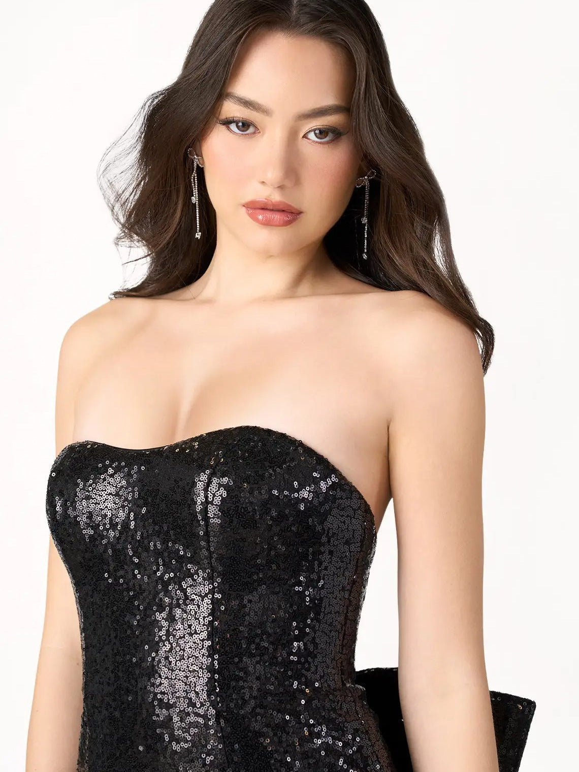 Close-up of the upper body of a woman wearing a black sequin strapless dress, against a white background.