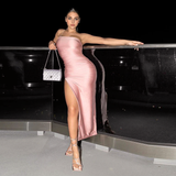 Woman in a pink ruched one-shoulder dress with a high slit, posing outdoors at night