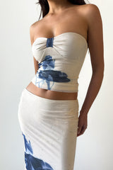 Close-up of a woman wearing a cream strapless top with a blue floral print and a matching cream maxi skirt with a blue floral print.