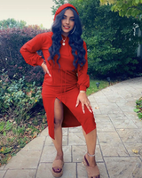 A woman in a red hooded midi dress with a high slit, platform sandals, and hoop earrings, standing outdoors on a paved path.