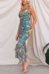 Side view of a woman in a green floral ruched midi dress with a ruffled mermaid hem.