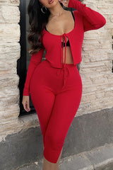 A woman in a red two-piece outfit stands in front of a brick wall. The outfit includes a cropped, tie-front top and matching pants.