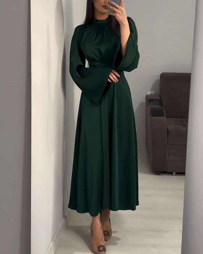 Woman wearing a long, dark green satin dress with bell sleeves and a wide belt, standing in front of a mirror.
