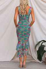 Back view of a woman in a green floral ruched midi dress with a ruffled mermaid hem.