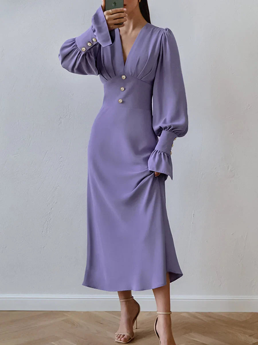 Woman wearing a long-sleeved purple dress with puffed sleeves and a V-neckline, standing and holding the skirt.