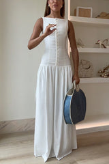 Woman in a white maxi dress adjusting her dress and holding a round blue and white straw bag