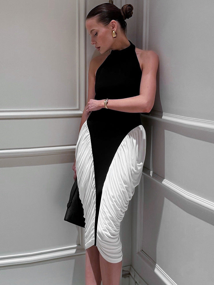 A woman in a black and white halter neck dress with ruched white fabric on the skirt, leaning against a white wall with her eyes closed.