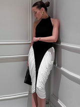 A woman in a black and white halter neck dress with ruched white fabric on the skirt, leaning against a white wall with her eyes closed.