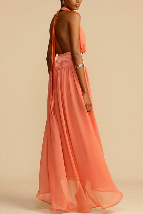 Back view of a model wearing a coral halter neck maxi dress with an open back and a long flowing skirt.