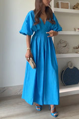 Woman posing in a blue maxi dress and gold clutch, showcasing the pleats.