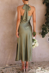 Woman in olive green satin slip dress with a halter neck and high slit, holding a bouquet of white flowers.
